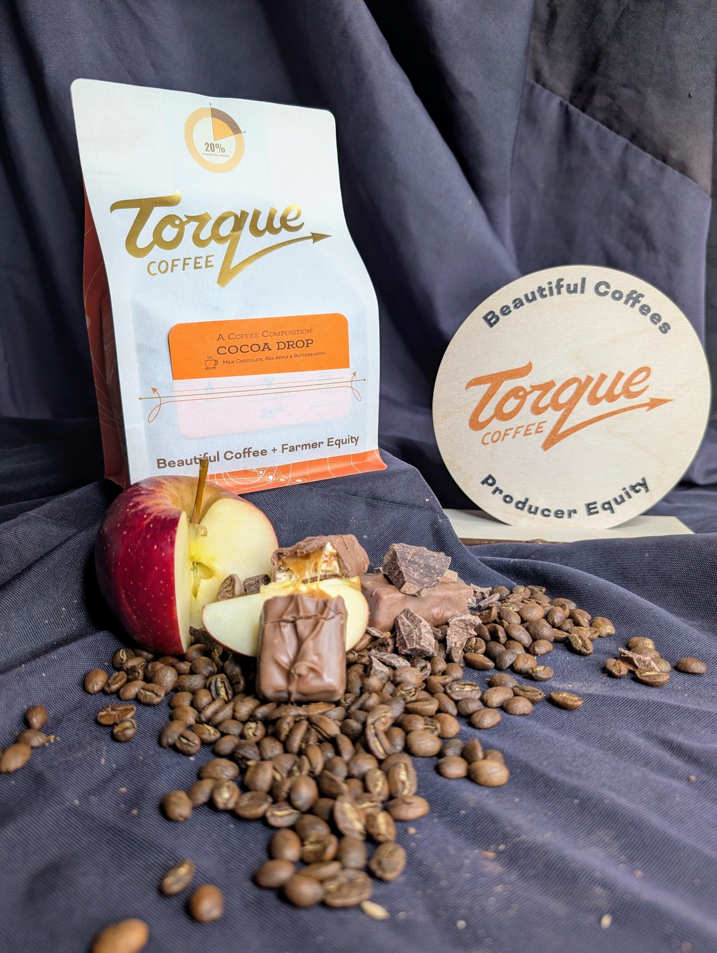 Torque Coffee package with coffee beans, chocolate, and an apple on a dark fabric background
