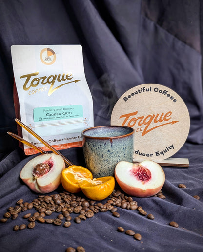 Torque Coffee package with coffee beans, peaches, and a coaster on a dark fabric background